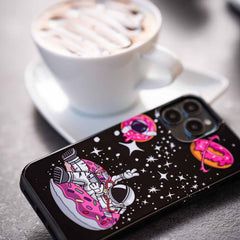 Schwarze Handyhülle mit Astronaut auf Donut und Weltraum-Motiv neben einer Tasse Kaffee